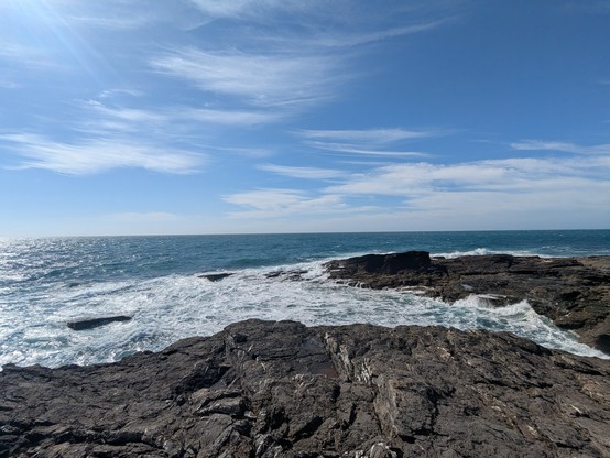 Looking out to see (approximately South) at Hook Lighthouse. In the foreground some dark rock, in the mid ground some azure sea and at the top, a bright blue sky