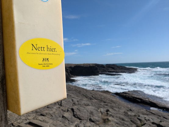 A Baden Württemberg "Nett Hier" sticker on the side of a plastic life buoy holder. 
The Atlantic sea in the background 