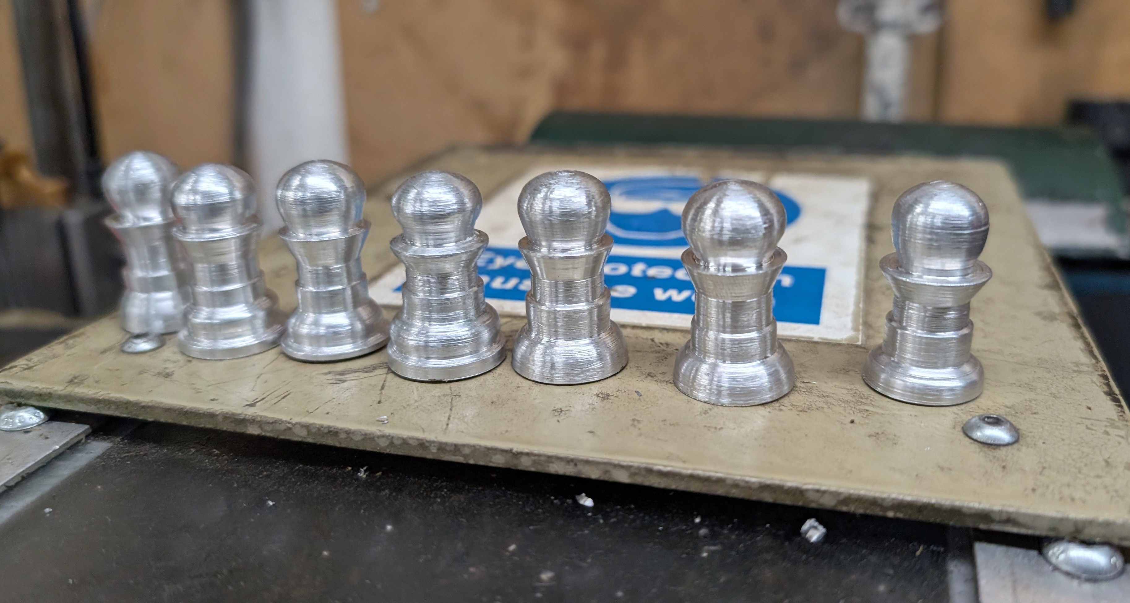 7 pawns lined up, turned out of aluminium. They're almost but not quite identical